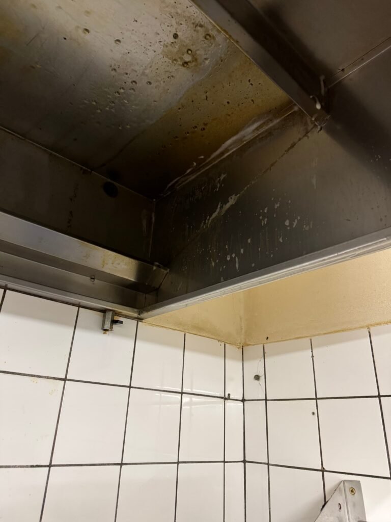 Verschmutzte Dunstabzugshaube mit Fettablagerungen und nassen Stellen über gefliester Küchenwand.