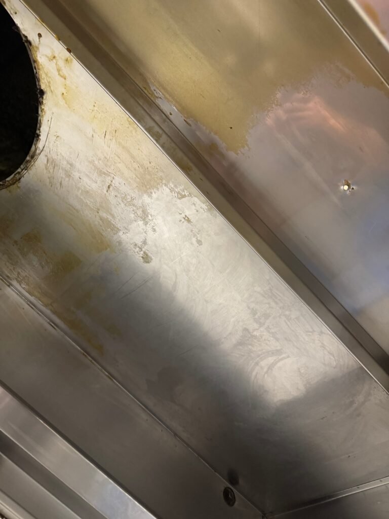 Verschmutzte Dunstabzugshaube mit Fettablagerungen und nassen Stellen über Küchenwand.