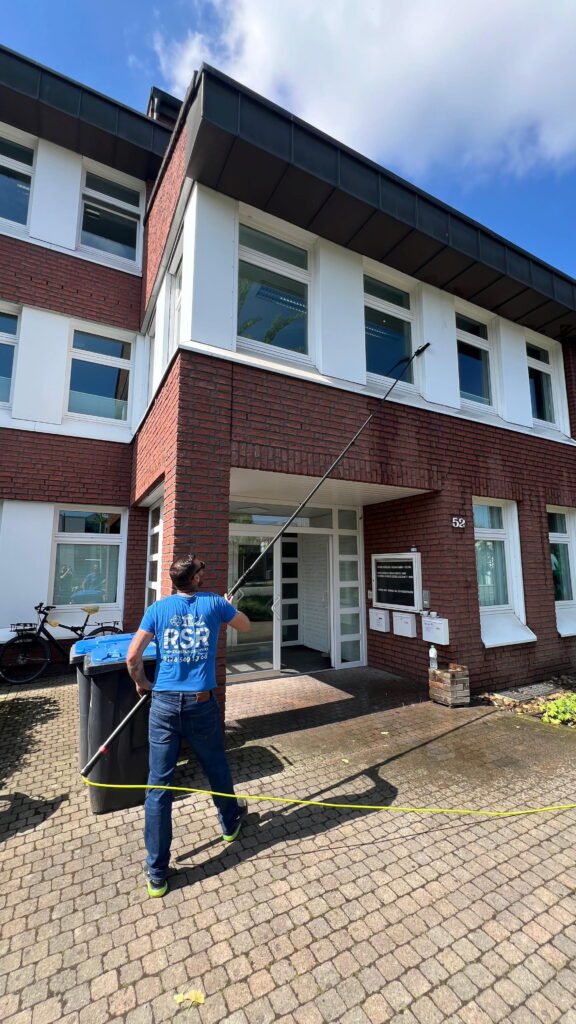 rsr-aussenreinigung-beim-kunde Mitarbeiter von RSR Münster reinigt die Fassade eines Bürogebäudes mit einem Osmose-Reinigungssystem und Teleskopstange